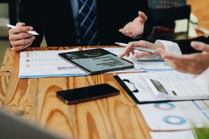 Close up diverse colleagues working on project together, sitting at table in boardroom, working with legal documents, financial report with statistics, employees engaged in teamwork at corporate meeting.